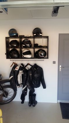 a motorcycle is parked in front of a wall mounted helmet rack with two jackets on it