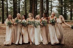 a group of women standing next to each other in front of some trees and holding bouquets