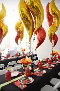 the table is set up with black and red tables cloths, silver chairs, and gold foil balloons