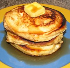 a stack of pancakes on a blue plate topped with a butter cube and some syrup