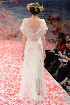 a woman walking down a runway in a white dress with flowers on the skirt and headpiece