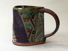 a coffee mug with dragonflies on it sitting on a white table top next to the words pottery by helene