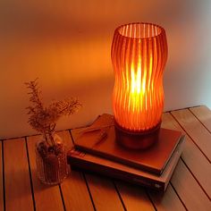 an orange lamp sitting on top of a wooden table next to a book and plant