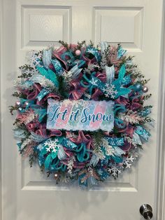 a wreath that says let it snow on the front door with blue and pink ribbons