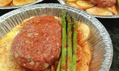 several tin plates with different types of food in them and asparagus on the side