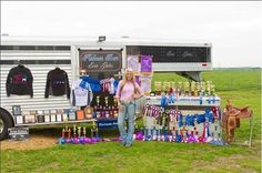 a woman standing in front of a horse trailer with merchandise for sale on the side