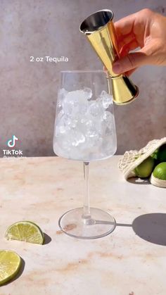 a person is pouring a drink into a glass with limes on the table next to it