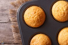 four yellow muffins in a black tray on a wooden table