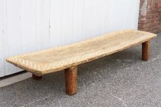 a wooden bench sitting in front of a white wall with a brick building behind it