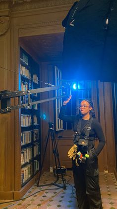 a woman standing in front of a book shelf with a camera and light on it