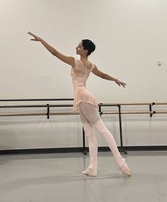 a ballerina in a ballet studio stretching her arms out to the side with one hand