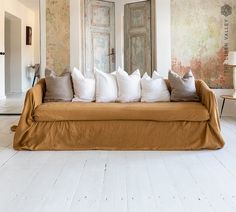 a couch with many pillows on it in front of two doors and a wall painting