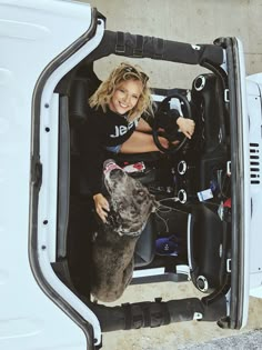 a woman sitting in the driver's seat of a white truck with a dog