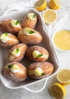 lemon filled doughnuts in a white dish next to sliced lemons and orange juice