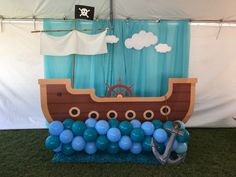 there is a fake boat with balloons on the grass and blue balls in front of it