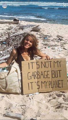 a woman sitting on the beach holding a sign that says it's not my garage but it's my planet