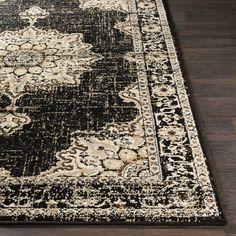 a black and beige area rug with an ornate design on the bottom, in front of a wooden floor