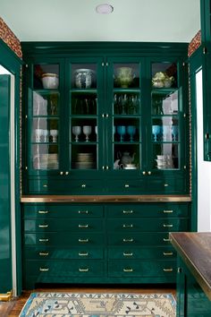 a green cabinet with glass doors and gold trim on the bottom, in a kitchen