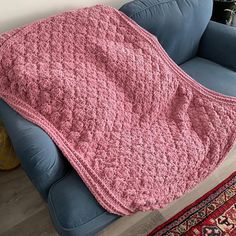 a pink crocheted blanket sitting on top of a blue couch next to a rug