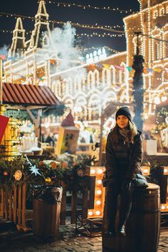 a woman sitting on top of a barrel in front of a building with christmas lights