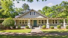 a gray house with white trim and blue door in the front yard is surrounded by trees