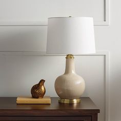 a white lamp sitting on top of a table next to a book and a vase