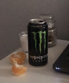 a can of monster energy drink next to an orange peel and a laptop on a table