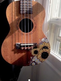 a ukulele with sunflowers painted on it sitting in front of a window