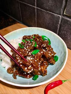 a plate with meat, rice and chopsticks on it next to a red chili pepper