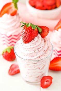 two cups filled with whipped cream and strawberries on top of each cup, sitting next to another glass bowl full of strawberries