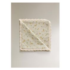 a white and yellow flowered blanket with lace trim on the edges, hanging from a wall