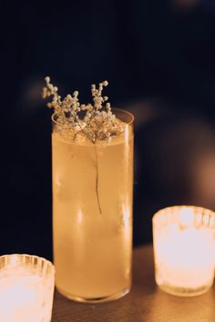 a glass with some flowers in it sitting on a table next to two lit candles