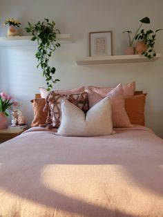 a bed with lots of pillows and some plants on the headboard in front of it