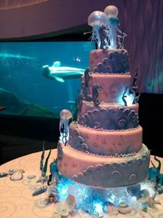 a three tiered cake with sea animals on it in front of a fish tank