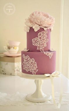 a three tiered cake with pink flowers on the top and white ribbons around it