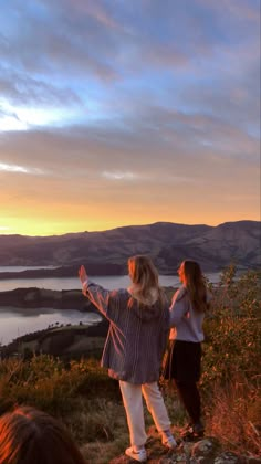 two women standing on top of a hill with their arms outstretched in front of the sun