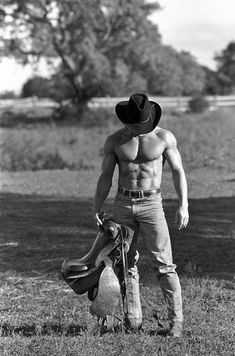 a shirtless man standing in the grass with his hat on