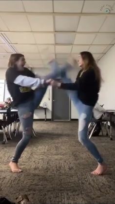 two people are dancing in an empty room with chairs and desks behind them, one is holding the other's leg