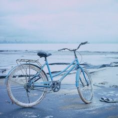 a blue bicycle parked on the beach in front of some water and ice covered rocks