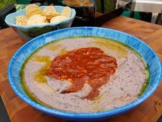 a blue bowl filled with dip and chips on top of a wooden table next to bowls of crackers