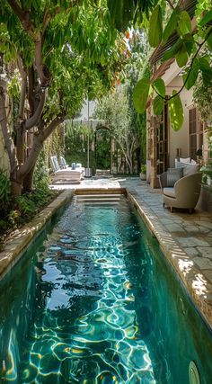 an outdoor swimming pool surrounded by trees and greenery, with lounge chairs in the background