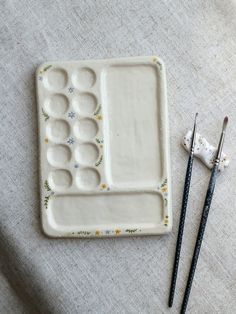 two chopsticks are next to a ceramic tray with holes in it and one is empty