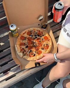 a person holding a pizza in front of a box with sodas on the table