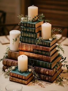 a stack of books sitting on top of a table next to candles and greenery