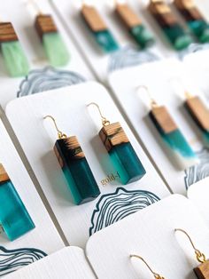 several pairs of wooden earrings are displayed in front of white cards with blue and green designs