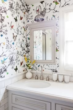 a bathroom sink with a mirror above it and wallpaper on the walls behind it