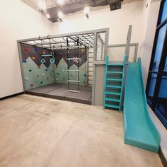 an indoor climbing wall and slide in a building with concrete floors, windows, and stairs