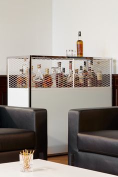 two black leather chairs sitting next to each other in front of a wall mounted liquor bottle rack