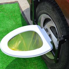 an open toilet seat on the grass next to a car door with its lid up