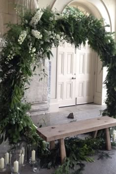 a wooden bench surrounded by greenery and candles in front of a white door with an arch